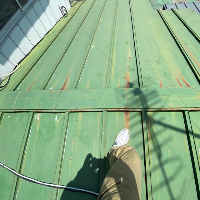 緑色のトタン屋根に登った作業員